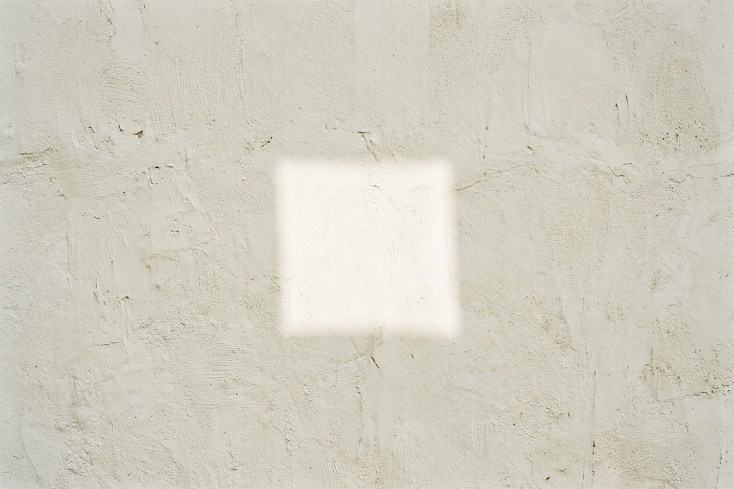 A blank lime washed wall in full sun carrying one bright square of light.