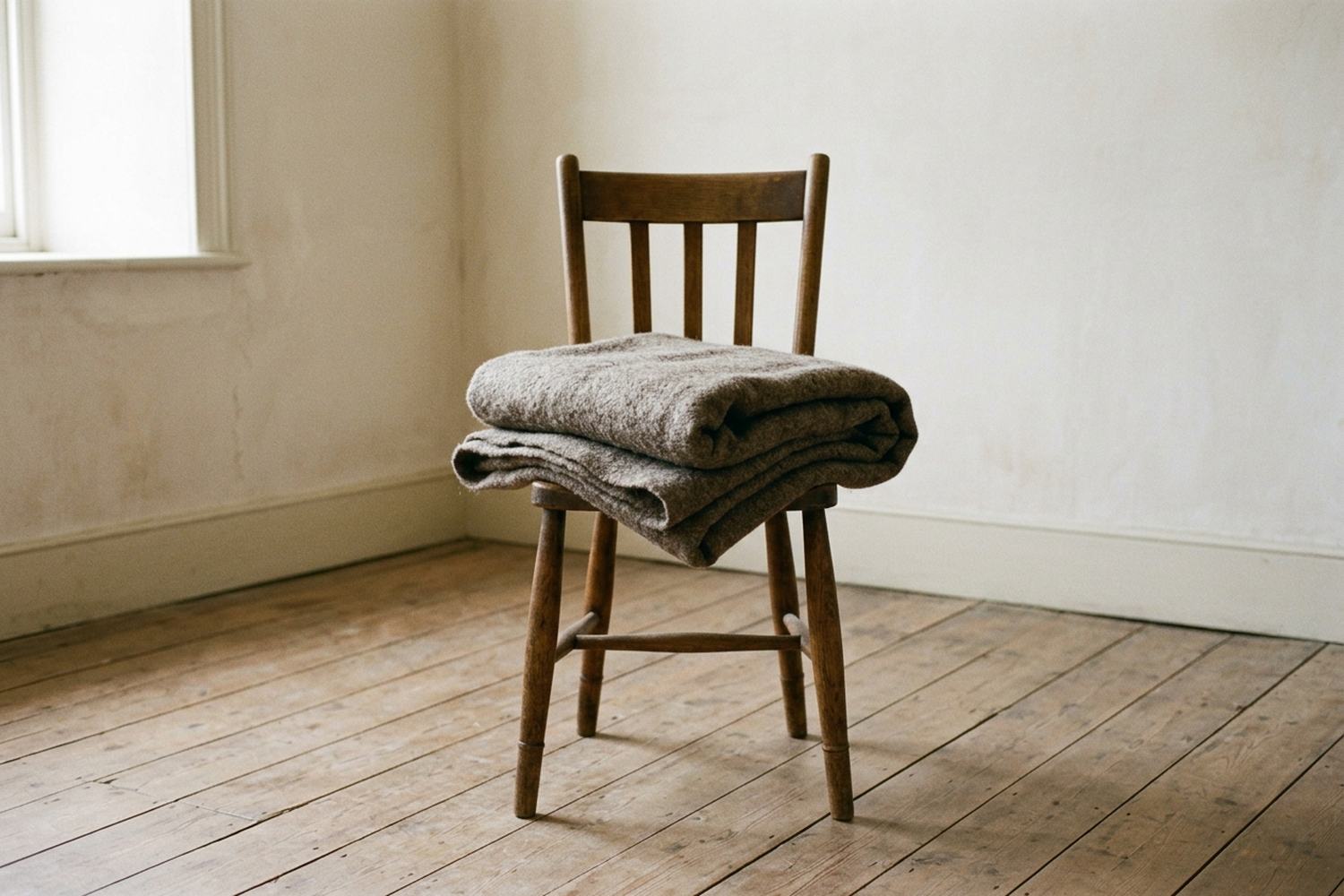One folded wool blanket on the seat of a plain wooden chair in an empty room.