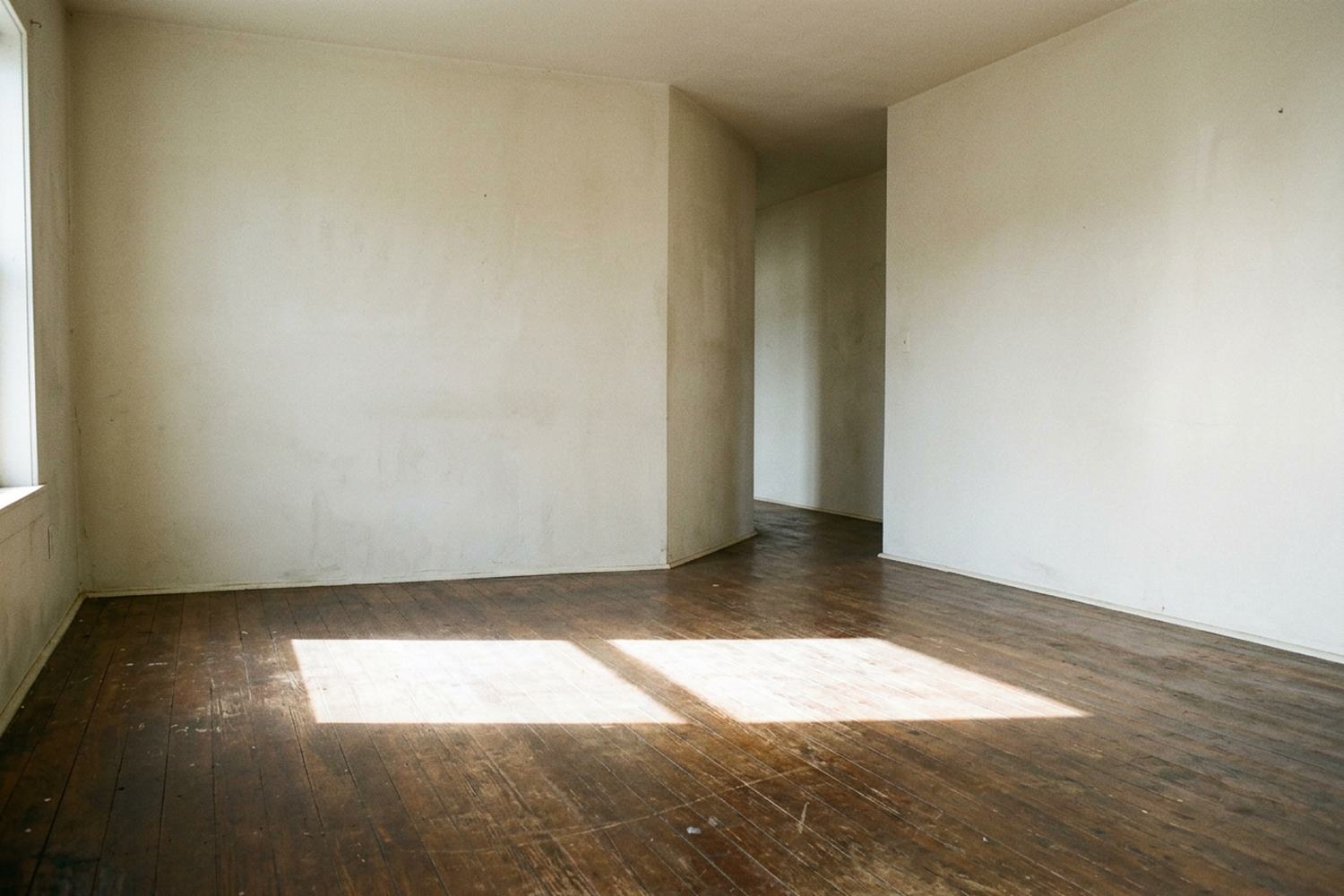 An empty room with a wide parallelogram of afternoon sun lying across the boards.