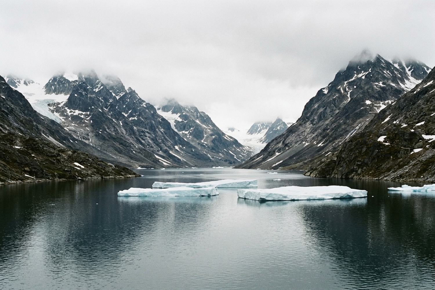 Still dark water between glaciated peaks with flat tabular ice on the surface.
