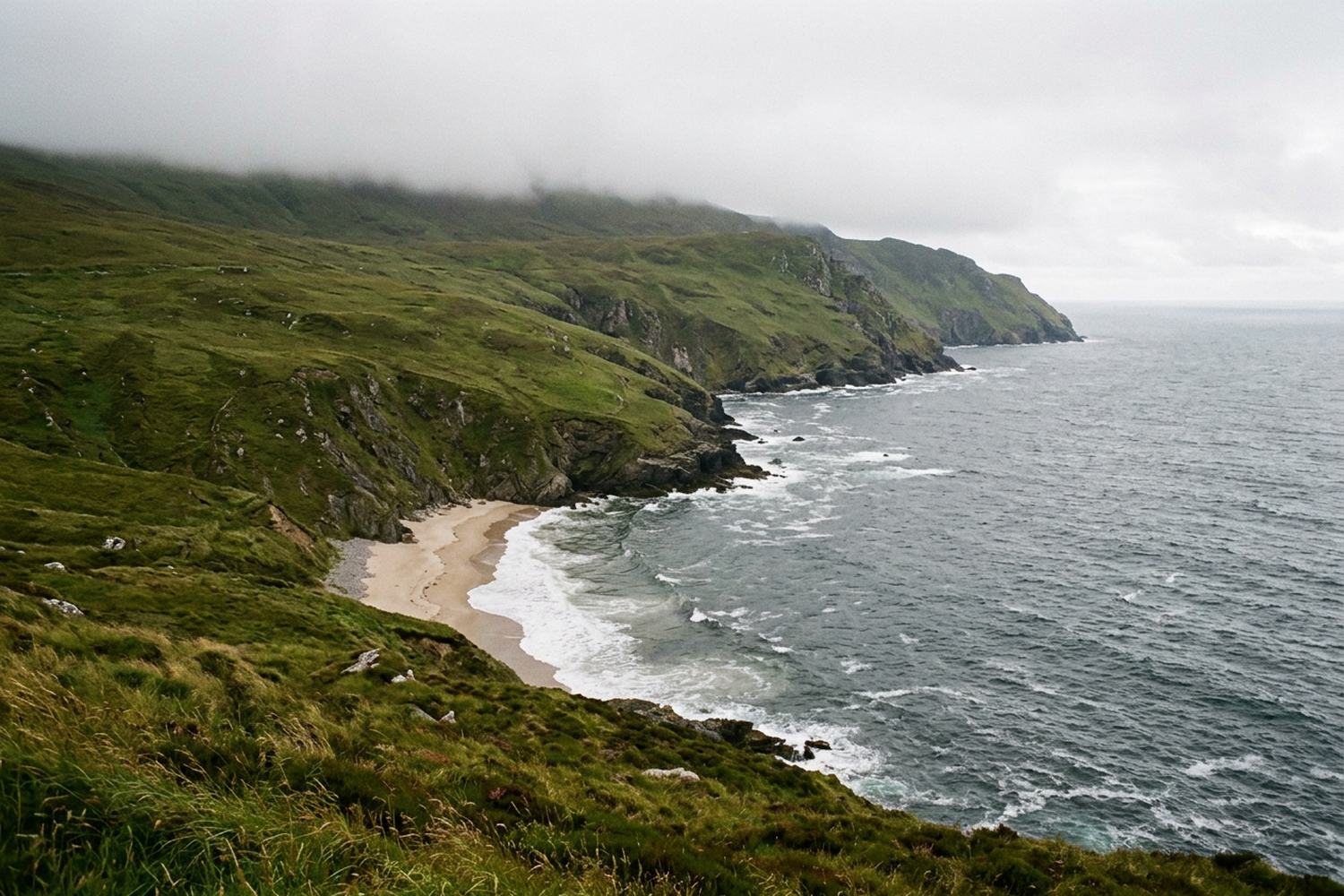 Steep grassy cliffs above a grey Atlantic with a crescent of sand far below.