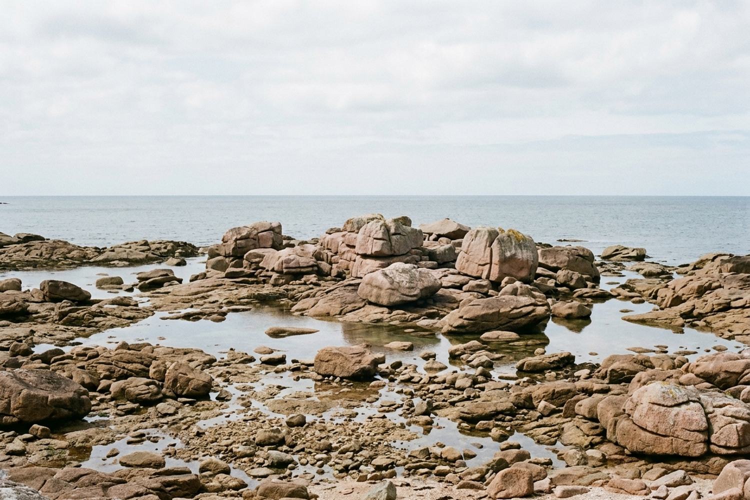 A tidal shore of pink granite boulders at low water with shallow pools between.